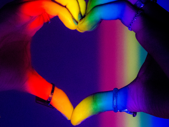 Herz geformt aus zwei Händen, in Regenbogenfarben angeleuchtet