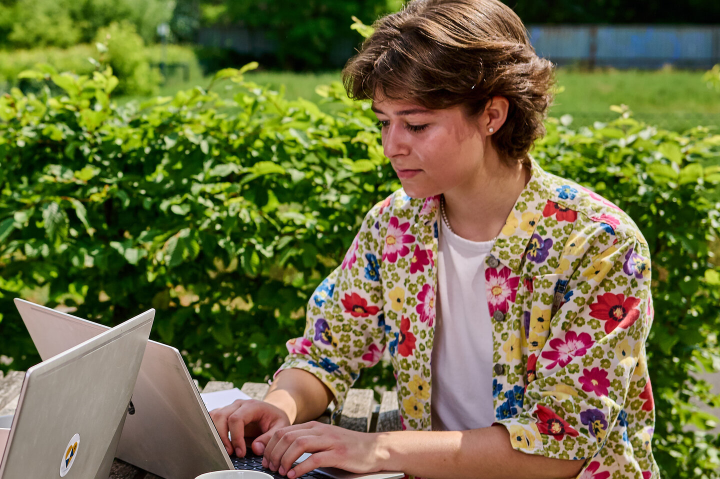 Zwei Studierende sitzen am Tisch im Innenhof der KHSB und arbeiten an ihren Laptops.