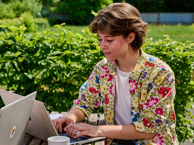 Zwei Studierende sitzen am Tisch im Innenhof der KHSB und arbeiten an ihren Laptops.