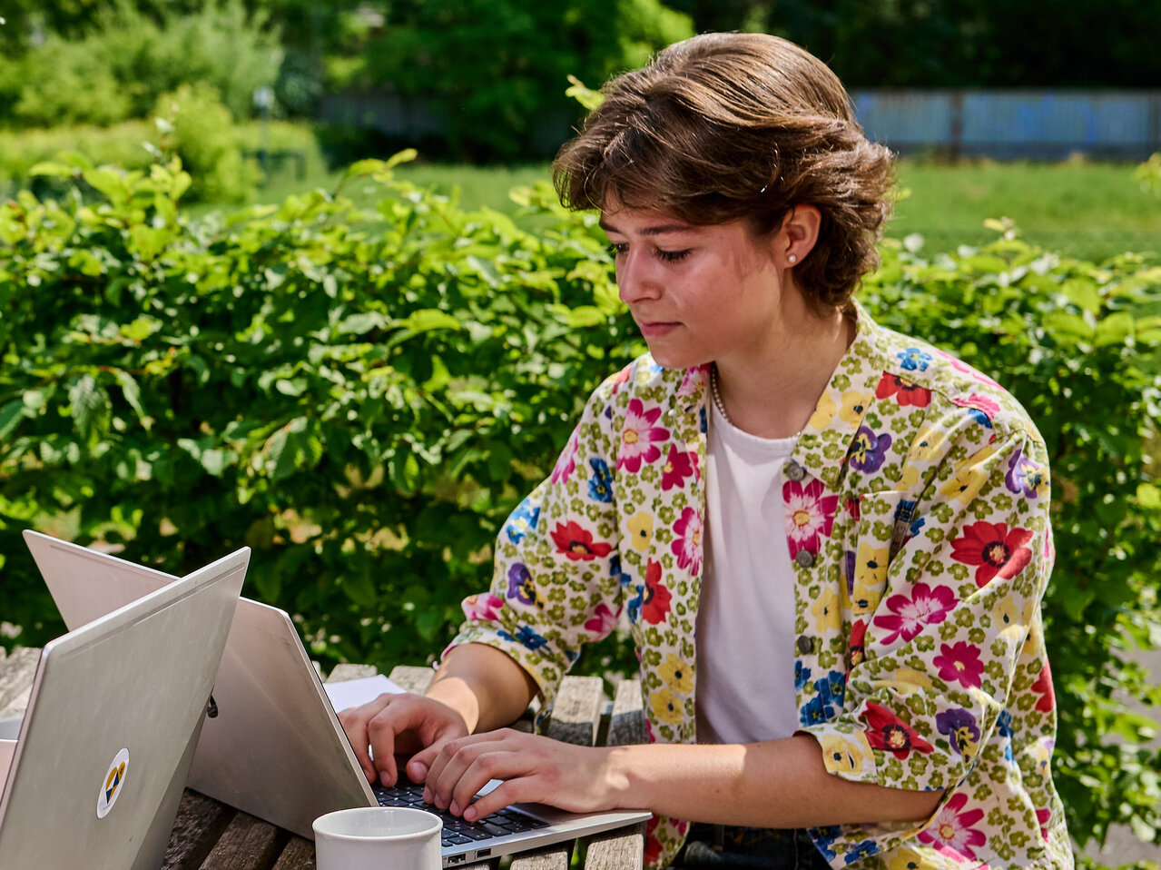 240527_KHSB_Karriere_Boillot_48 Zwei Studierende sitzen am Tisch im Innenhof der KHSB und arbeiten an ihren Laptops.
