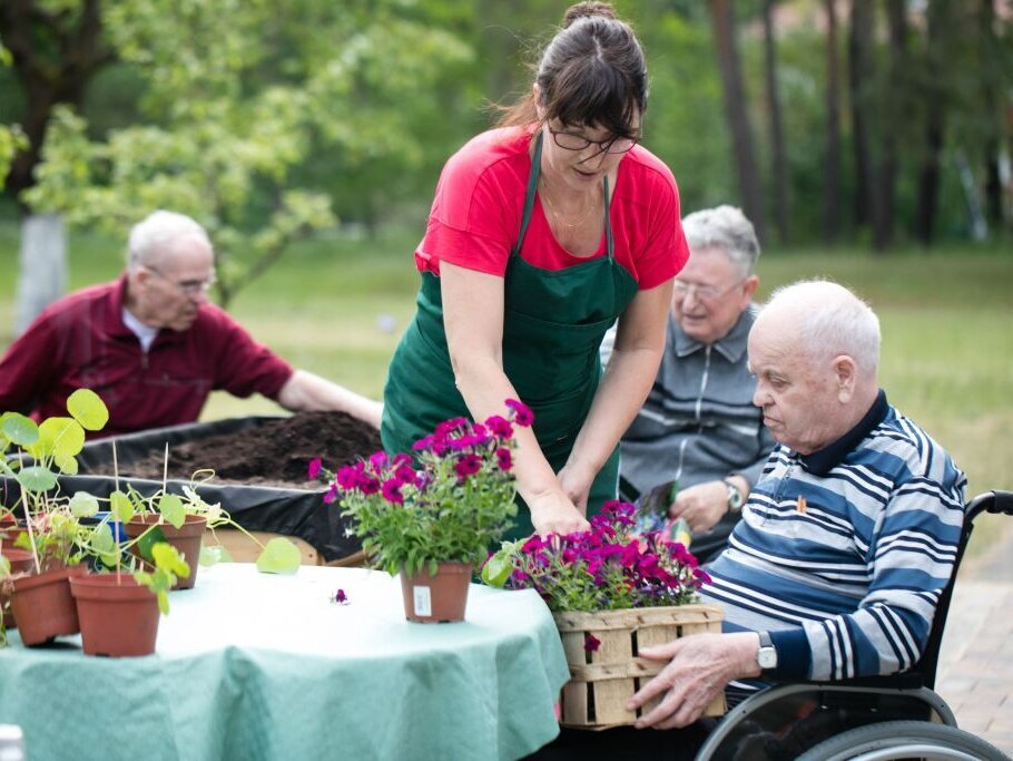 Gartentherapeutin pflanzt gemeinsam mit Senioren Blumen in die Hochbeete.