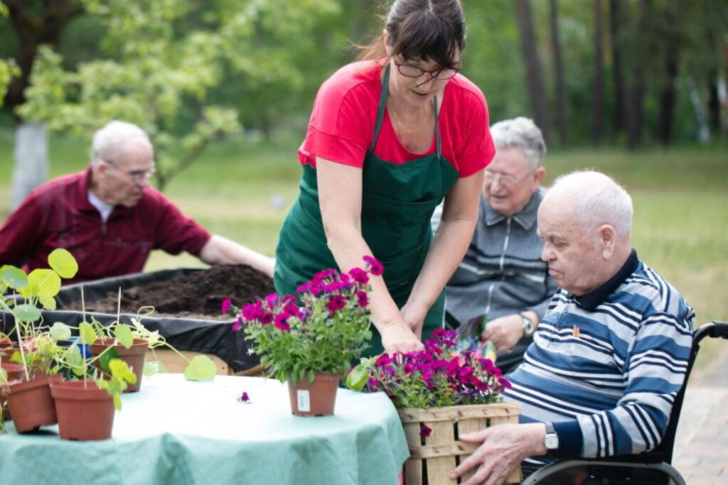 Gartentherapeutin pflanzt gemeinsam mit Senioren Blumen in die Hochbeete.