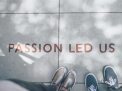 Vogelperspektive: zwei Menschen stehen auf Fußbodenplatten, nur die Schuhe sind sichtbar und der Schriftzug Passion led us