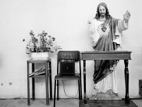 Symbolbild: Jesus-Statue mit Blumen und einem Verstärker