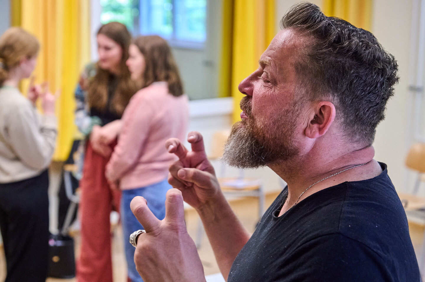 Der Dozent ist im Vordergrund zu sehen, während eine dreiköpfige Gruppe von Studierenden im Hintergrund Gebärdensprache übt.