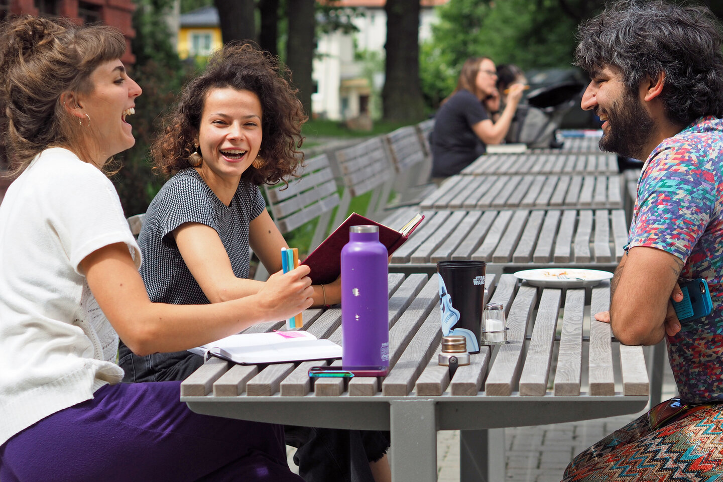 Studierende auf dem Campus, an Tischen vor der Mensa im Gespräch