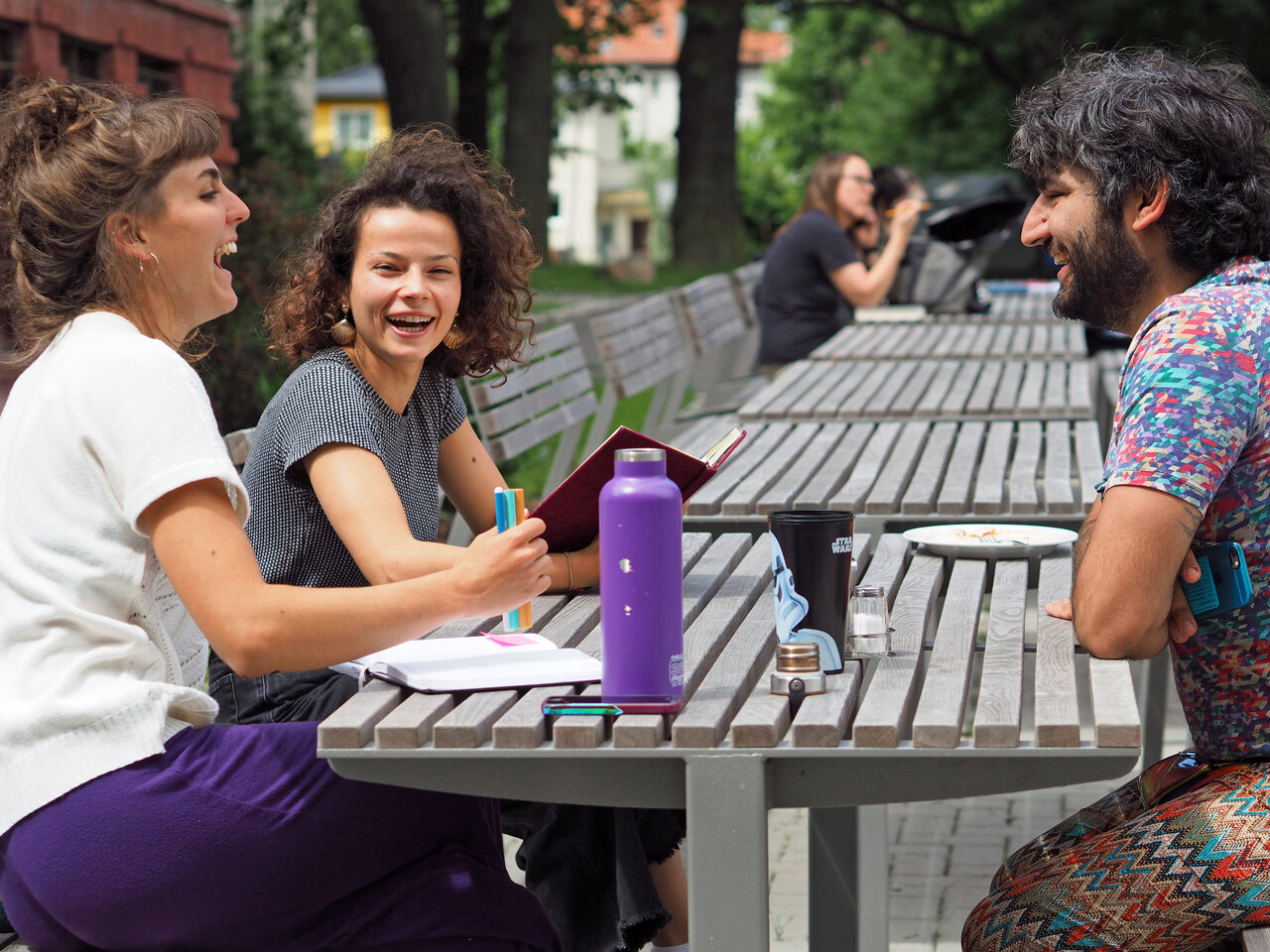 Studierende auf dem Campus, an Tischen vor der Mensa im Gespräch