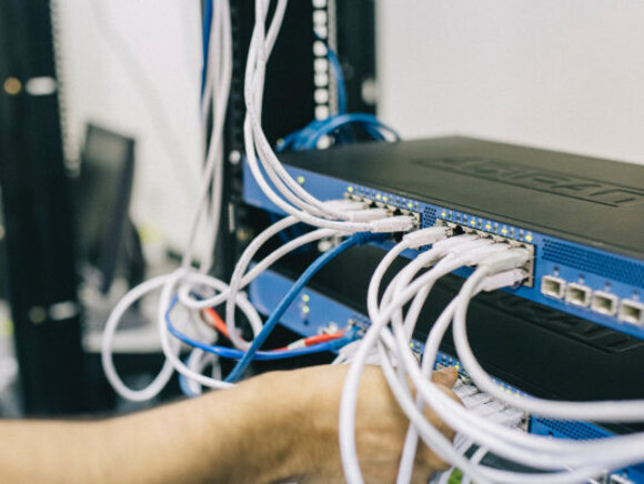 Eine Hand steckt eines von vielen Kabeln in einen Server