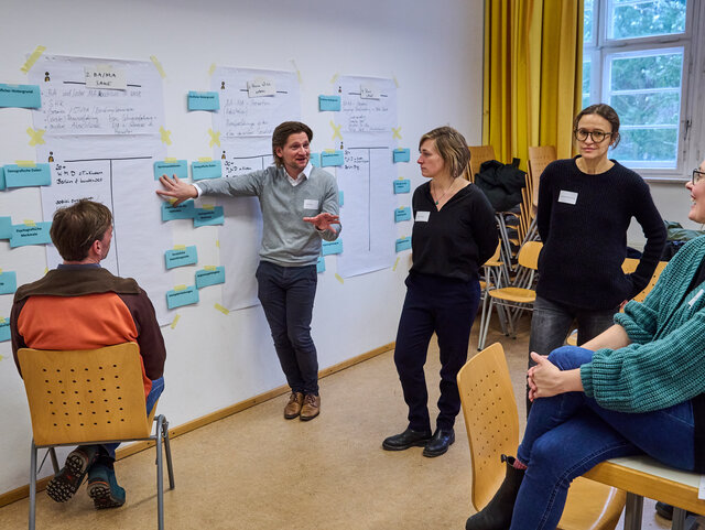 Workshop-Teilnehmende stehen zusammen und besprechen ihre Ideen.