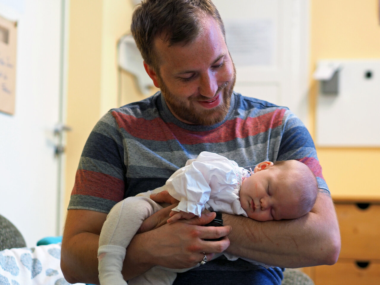 Ein Student hält sein schlafendes Baby im Arm. 
