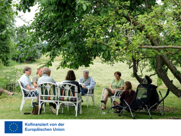 Eine Gruppe älterer Menschen sitzt unter einem Baum im Garten.