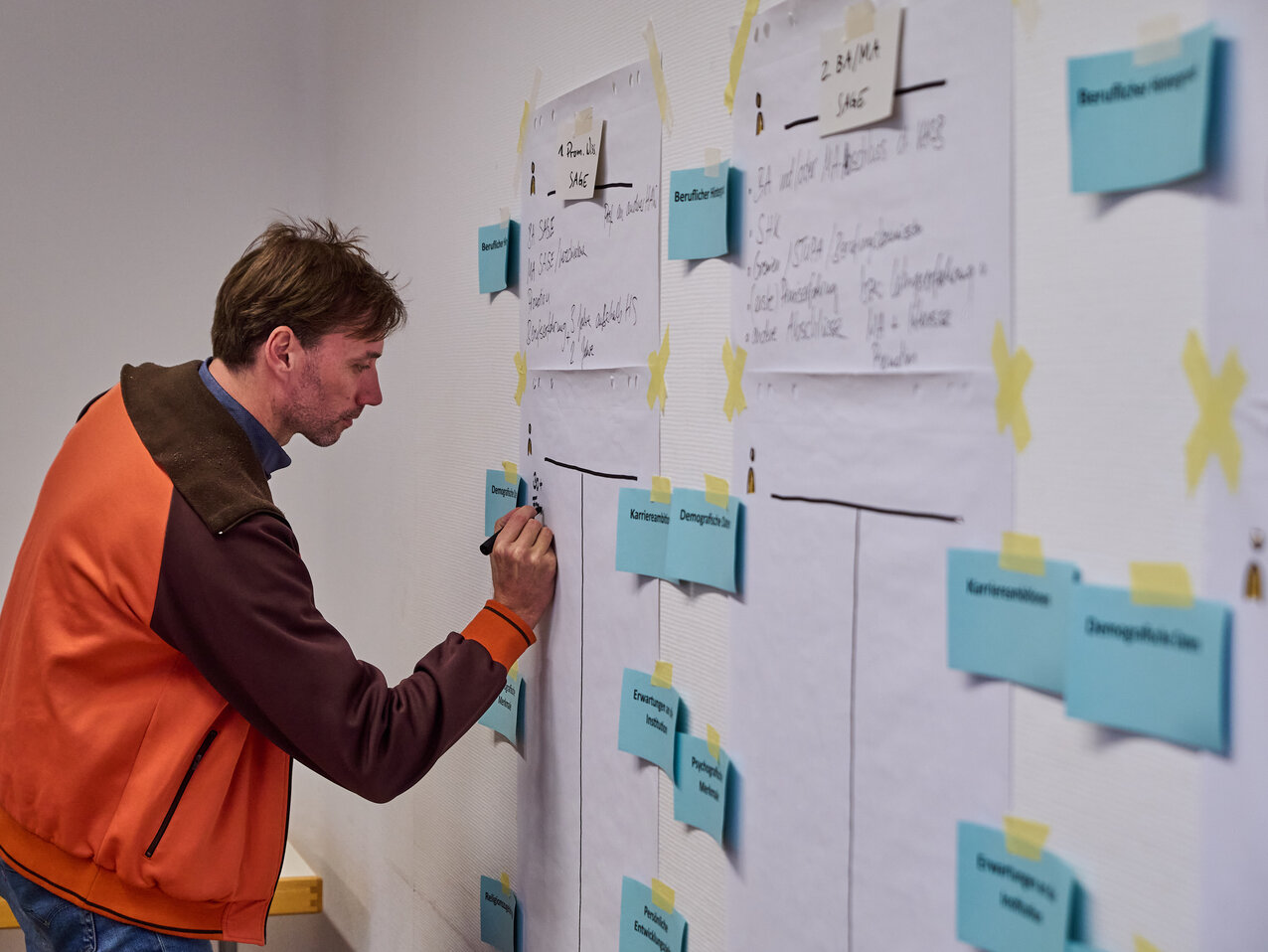 231129_KHSB_Workshop_Boillot_19 Ein Workshop-Teilnehmender notiert etwas auf einer großen Pinnwand mit Ideen.