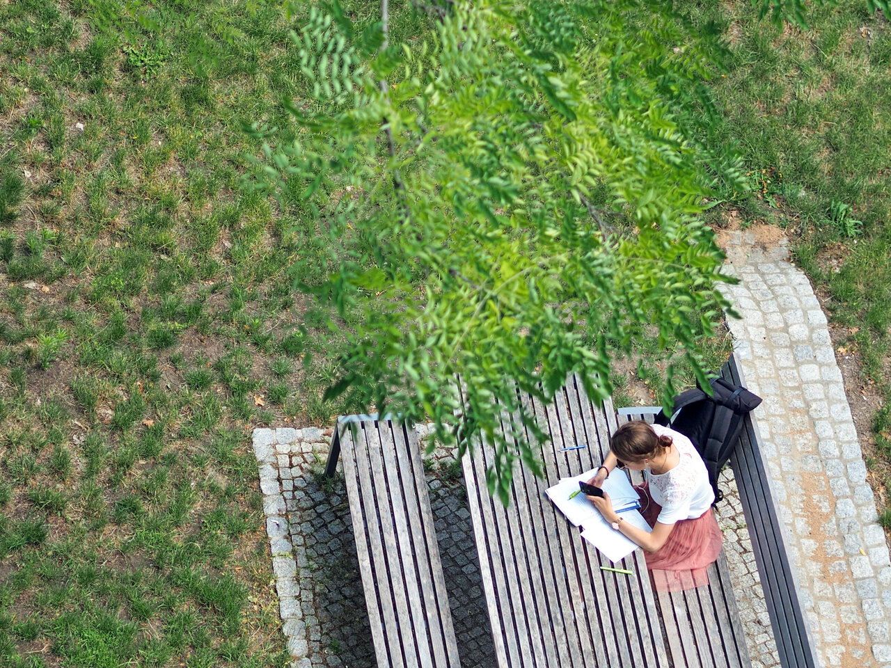 Eine Studierende sitzt an einer Bank im Innenhof der KHSB mit Unterlagen.