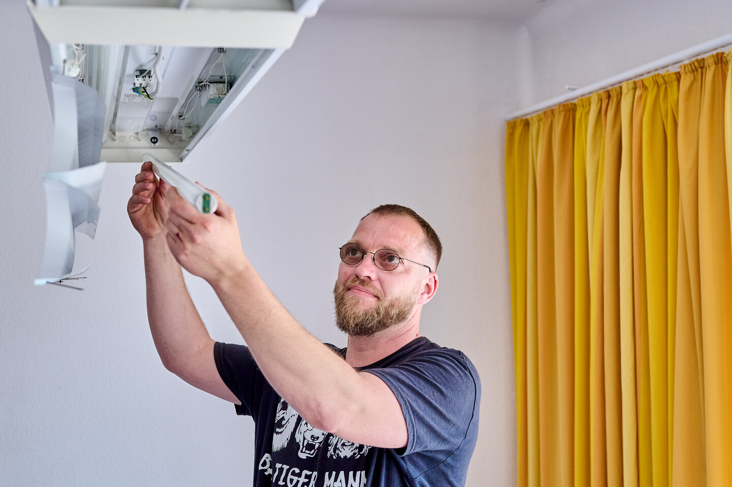Ein Mitarbeiter der KHSB wechselt die Leuchtstoffröhren einer Deckenlampe aus.