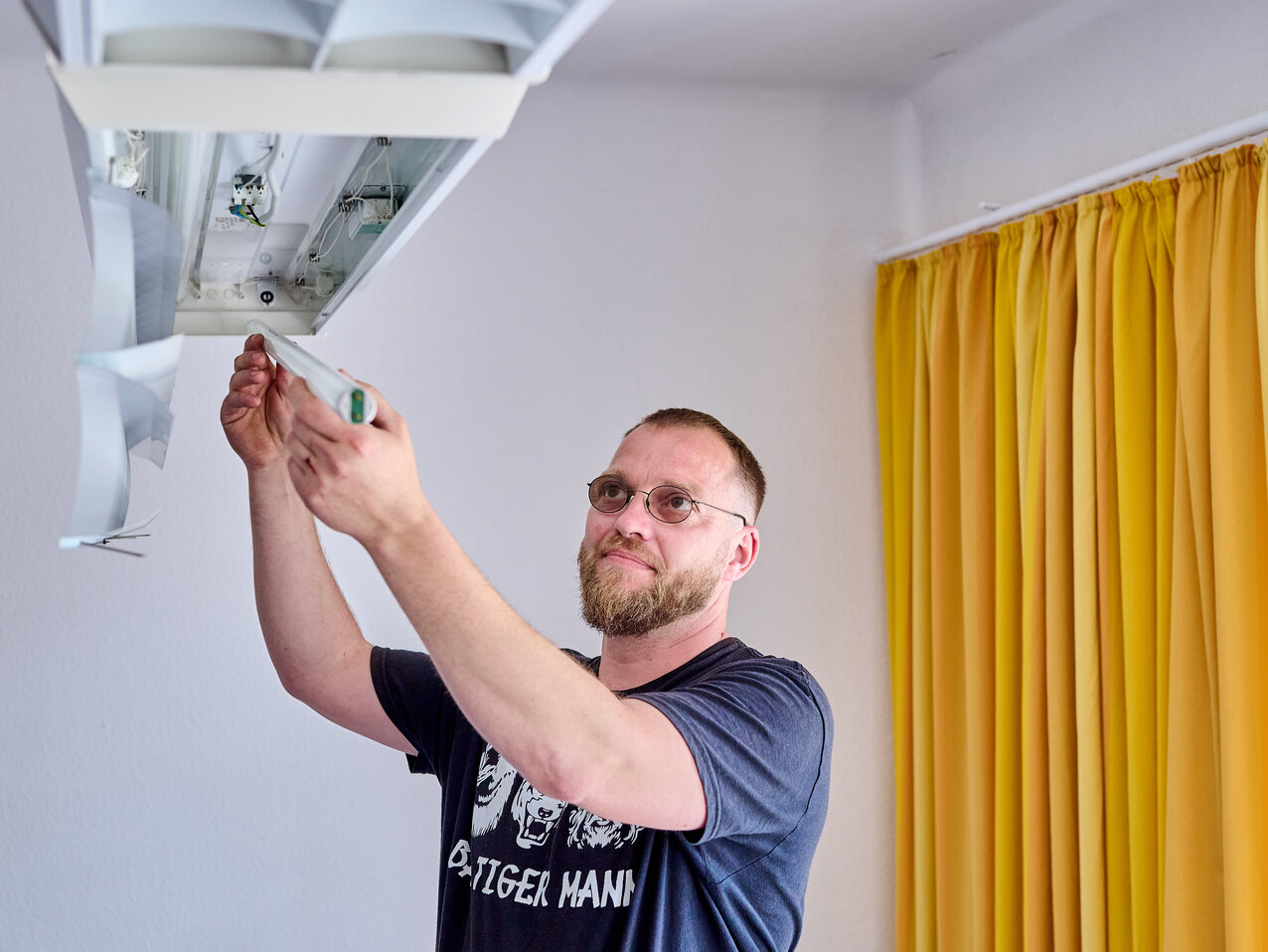 Ein Mitarbeiter der KHSB wechselt die Leuchtstoffröhren einer Deckenlampe aus.