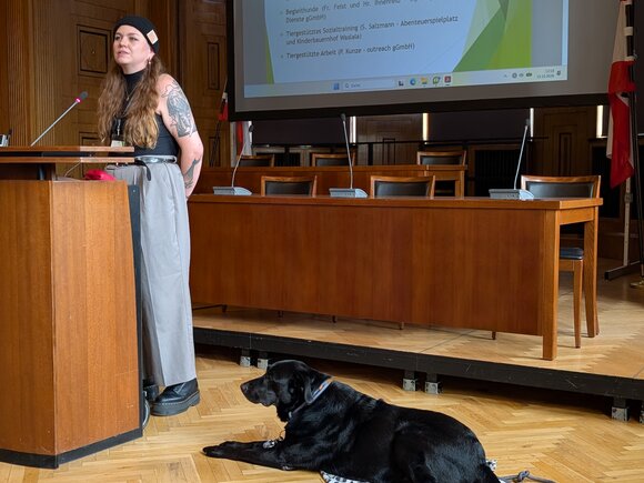 Sozialpädagogin Ann-Christin Feist berichtet über Tiergestützte Aktivitäten bei Ihrem Träger My Way Soziale Dienste, während Hund Max sie aufmerksam begleitet.