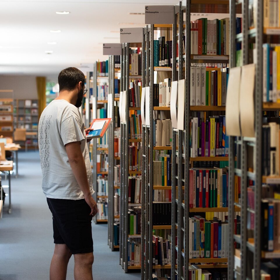 Bibliothek Studierender steht zwischen Bücherregalen