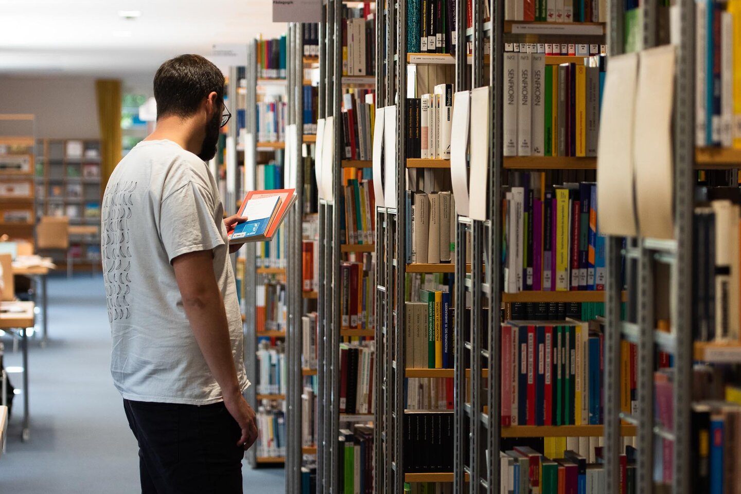 Bibliothek Studierender steht zwischen Bücherregalen