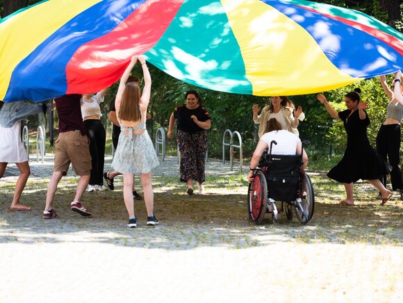 Eine Seminargruppe hält gemeinsam ein großes Schwingtuch hoch.