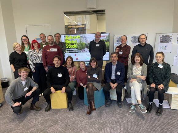 Gruppenbild der Teilnehmden vor einem Bildschirm mit der Aufschrift "Zukunft findet Stadt"