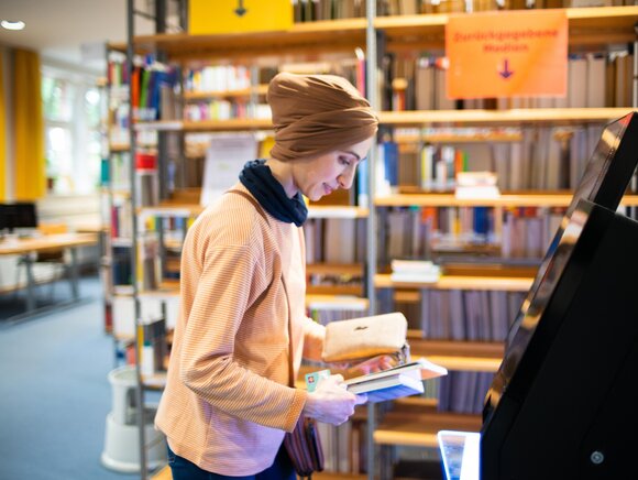 Eine Studentin leiht sich in der Bibliothek Bücher aus. 