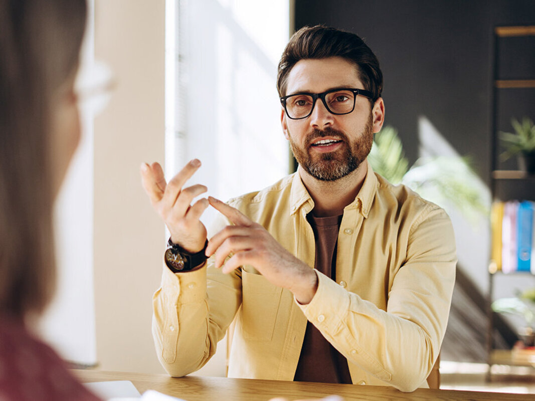 Mann unterhält sich mit einer Frau an einem Schreibtisch