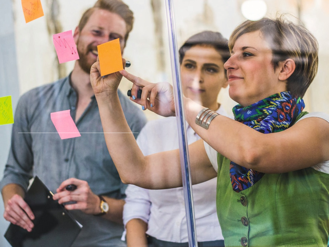 Personen stehen vor Glasscheibe und kleben Post-its