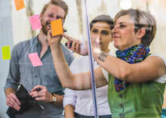 Personen stehen vor Glasscheibe und kleben Post-its