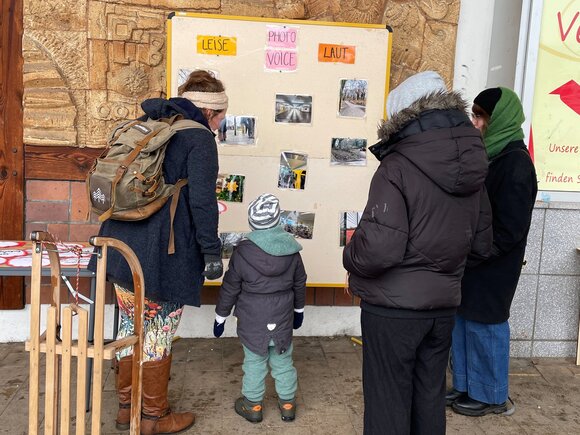 Eine Mutter mit Kind schauen sich eine Stellwand zum Thema "laute und leise Orte" an.