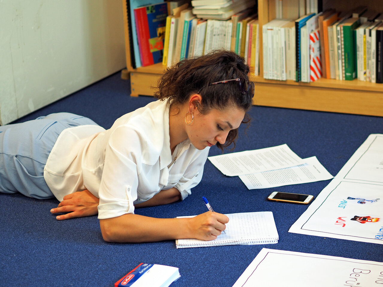 Eine Studierende liegt in der Bibliothek auf dem Boden und schreibt in ihr Notizbuch.