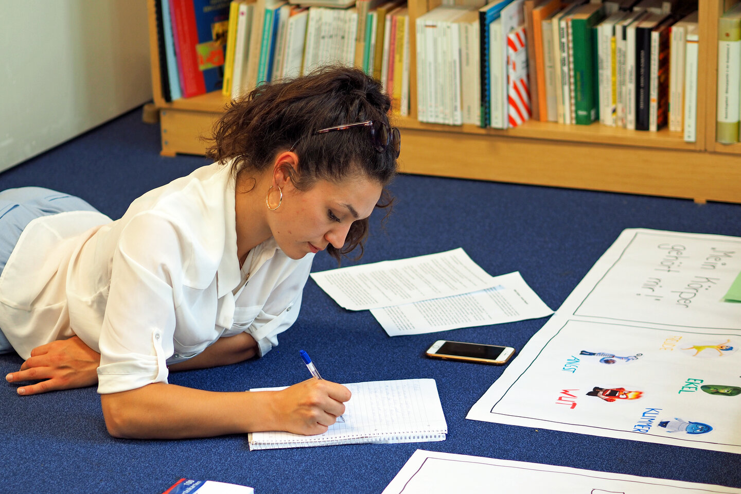 Eine Studierende liegt in der Bibliothek auf dem Boden und schreibt in ihr Notizbuch.