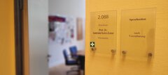 Ersthelferkreuz auf Türschild an der KHSB, im Hintergrund Büro