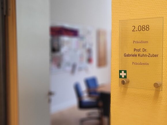 Ersthelferkreuz auf Türschild an der KHSB, im Hintergrund Büro