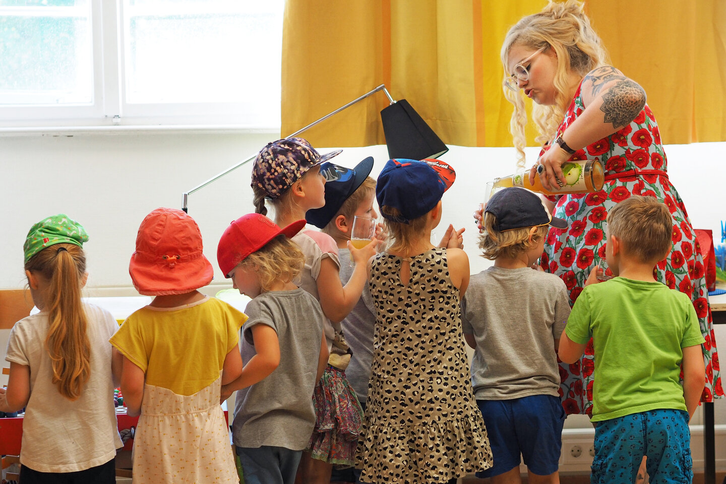 Eine Studentin gießt ein Getränk ein, während eine Gruppe Kinder um sie herumsteht.