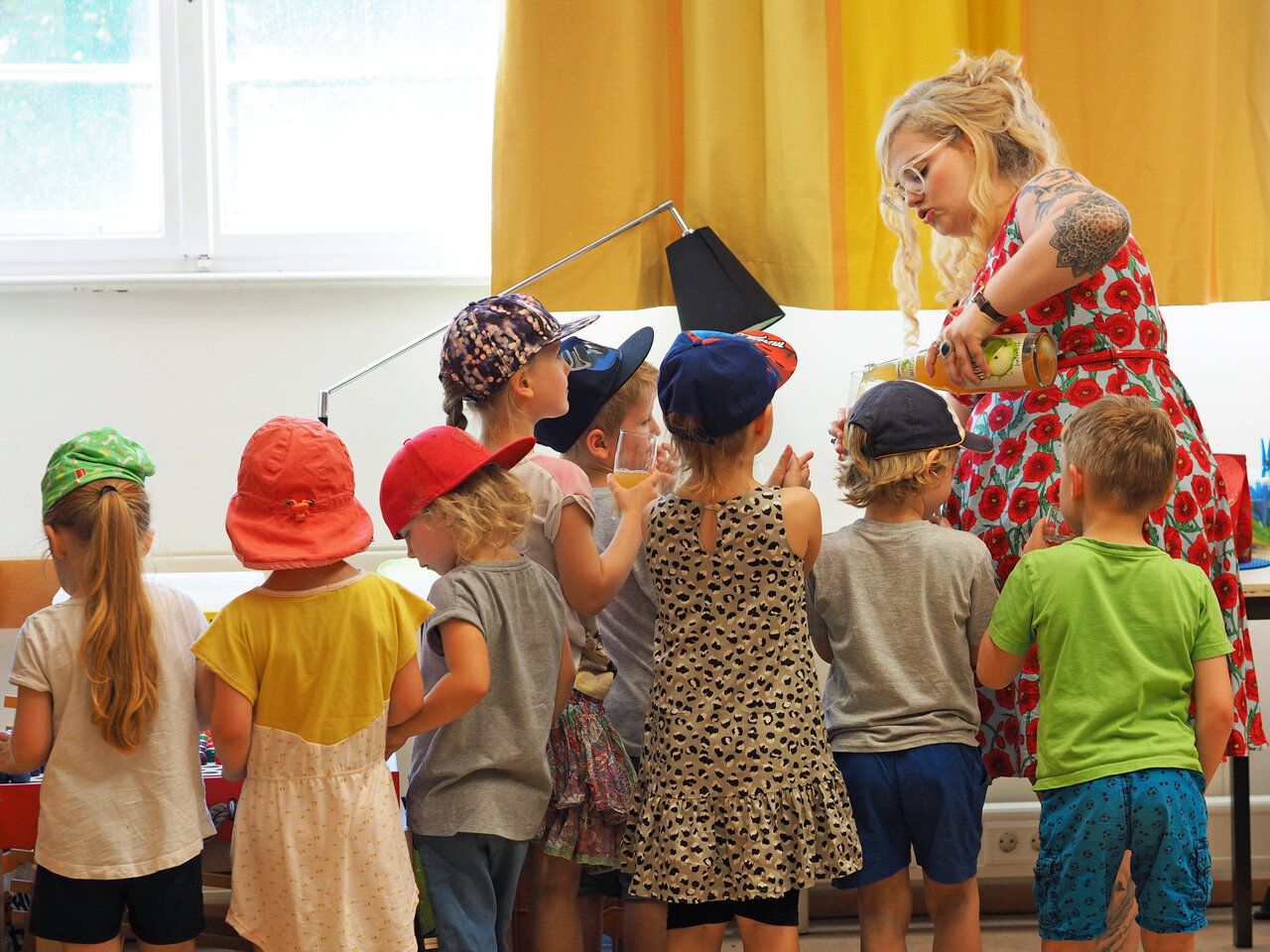 Eine Studentin gießt ein Getränk ein, während eine Gruppe Kinder um sie herumsteht.