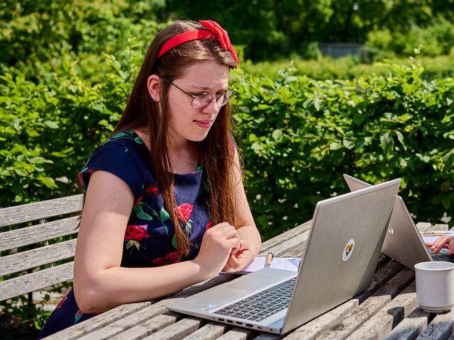 Zwei Studierende sitzen im KHSB Innenhof an einem Tisch mit ihren Laptops.