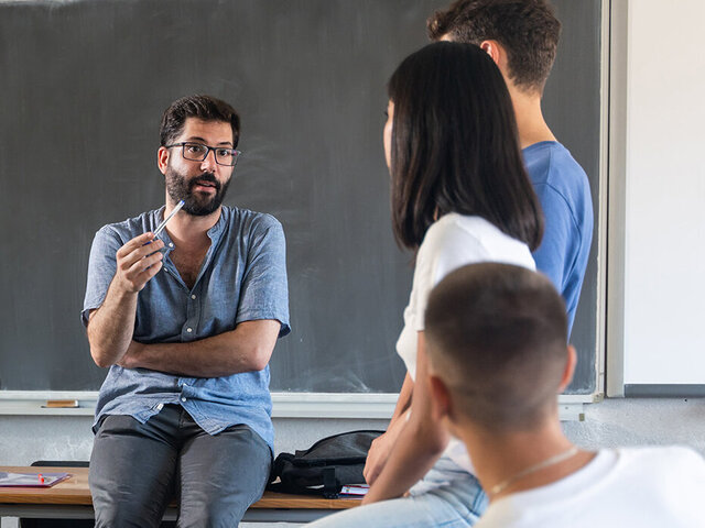Lehrer spricht mit Schüler*innen vor einer Tafel