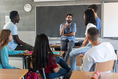 Lehrer spricht mit Schüler*innen vor einer Tafel