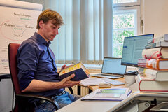 Ein Mitarbeiter der KHSB sitzt an seinem Schreibtisch und liest in einem Buch.