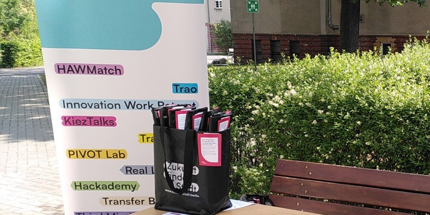 Hinter einem Tisch mit Infomaterialien steht ein Banner mit den Logos der einzelnen Teilvorhaben.