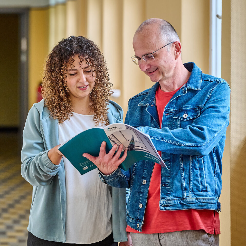 Zwei Mitarbeitende der KHSB stehen im Flur und betrachten eine Broschüre.