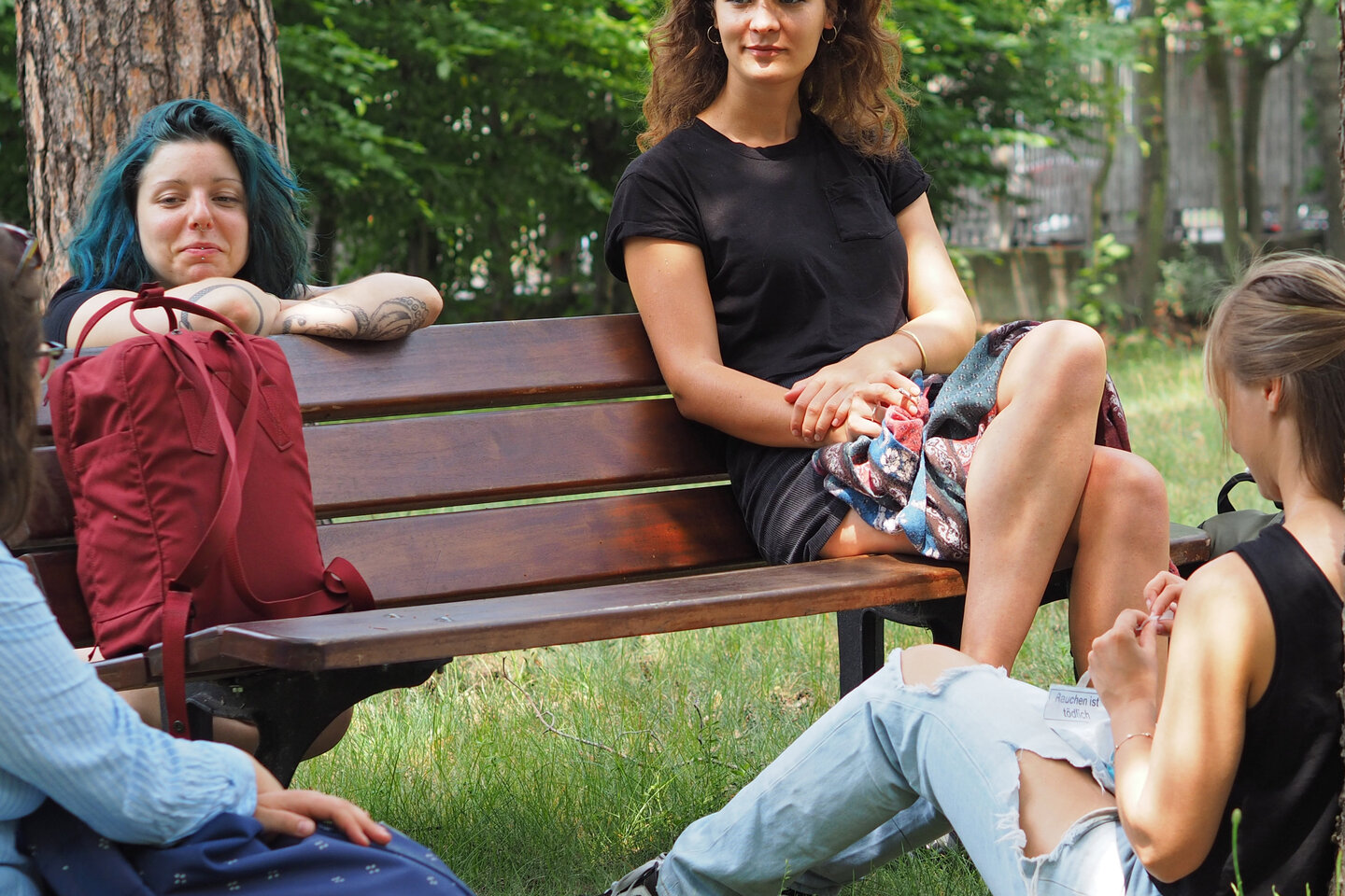 Studierende sitzen auf einer Bank und im Gras daneben und unterhalten sich. 