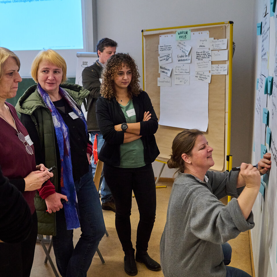 231129_KHSB_Workshop_Boillot_28 Mehrere Personen stehen nachdenklich vor Metaplan-Wänden und notieren ihre Gedanken auf Karten.