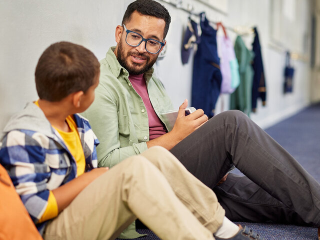 Erzieher spricht sitzend mit Kind in der Umkleide