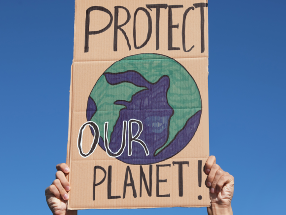 Hände halten Plakat mit Schriftzug Rettet den Planet und gemalter Erde in den Himmel