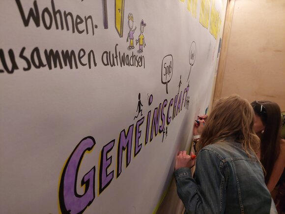 Zwei junge Menschen malen auf eine große Leinwand mit der Aufschrift "Gemeinschaft"