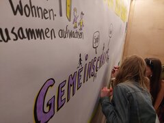 Zwei junge Menschen malen auf eine große Leinwand mit der Aufschrift "Gemeinschaft"
