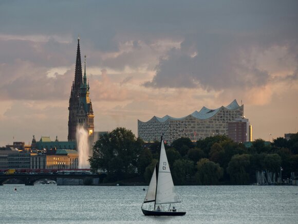 Weißes Segelboot tagsüber auf dem Wasser, im Hintergrund die Elbphilharmonie in Hamburg, das Hamburger Rathaus und ein Kirchturm